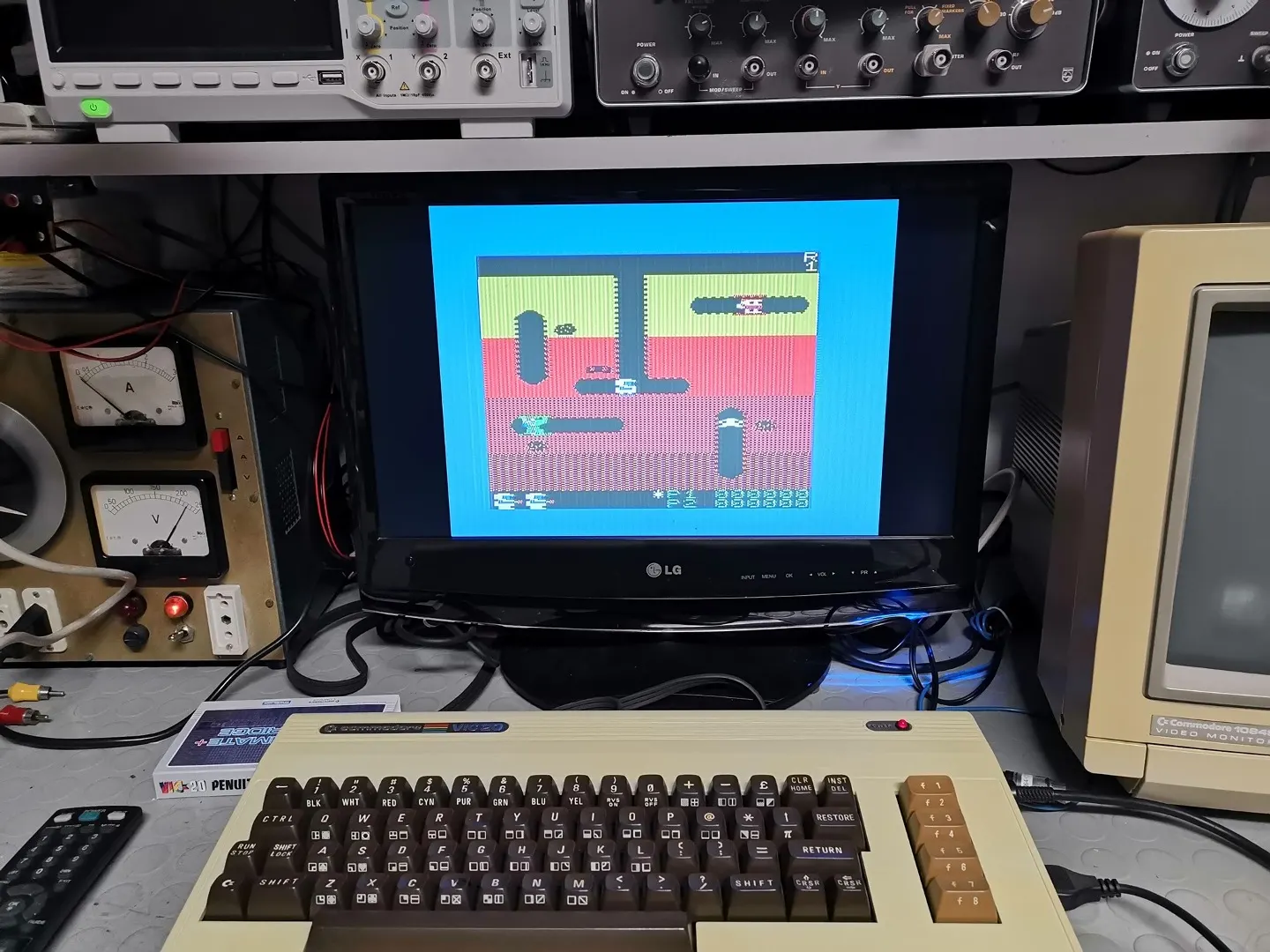 Un Commodore VIC-20 collegato a un monitor che mostra un videogioco a 8 bit, su un banco da laboratorio con strumenti di misura