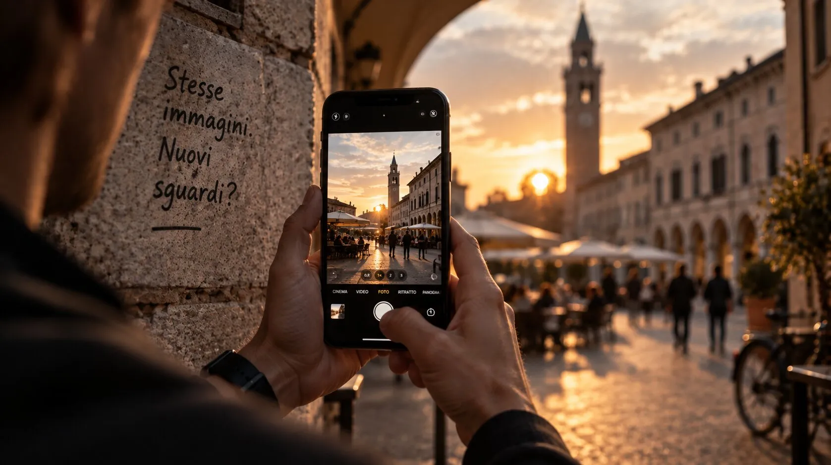 Due mani inquadrano con lo smartphone una piazza porticata con il campanile al tramonto; sul muro accanto, scritto a mano: «Stesse immagini. Nuovi sguardi?».