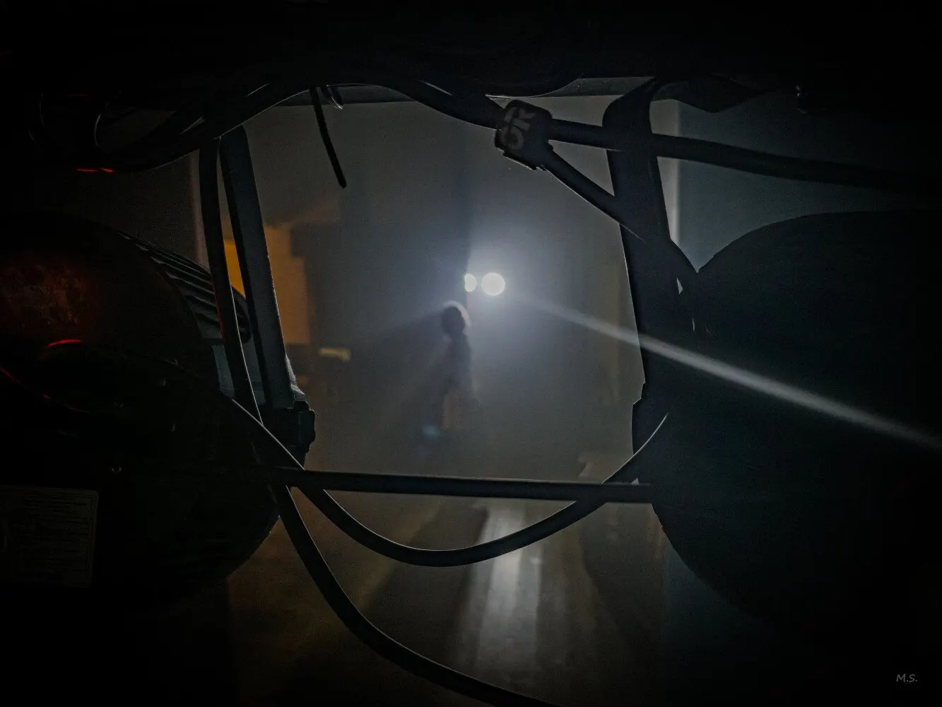 Dietro le quinte, tra cavi e fari di scena in controluce: in fondo, nella nebbia illuminata, la sagoma di un attore sul palco.